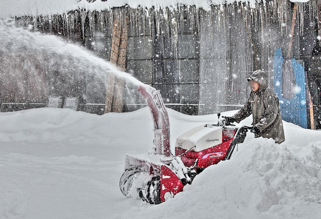 合掌造りの家の前を除雪する人物